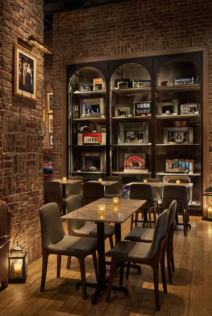 Cozy restaurant interior with brick walls, candle-lit tables, and a display of miniature stage dioramas on shelves.