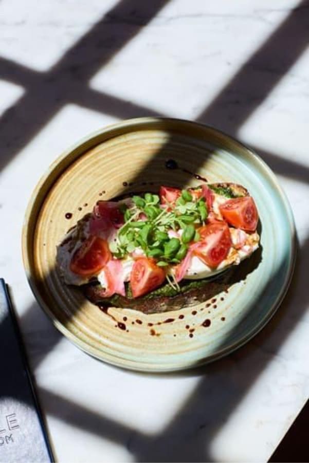 Open-faced toast topped with fresh tomatoes, greens, and cream on a ceramic plate